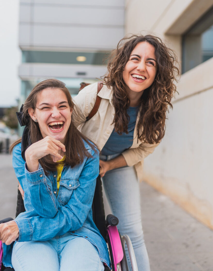 Young woman with cerebral palsy laughs with her personal assistant outdoors They share a candid and joyful moment on the sidewalk, concept of cerebral palsy