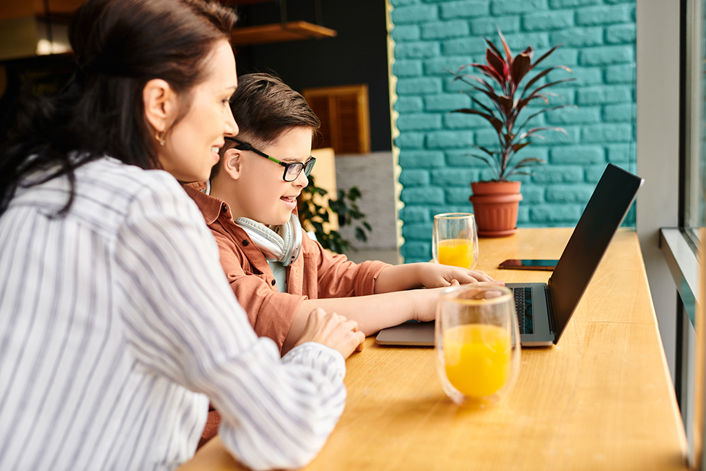 A mother and her son enjoy quality time together in a vibrant cafe, engaging with a laptop.