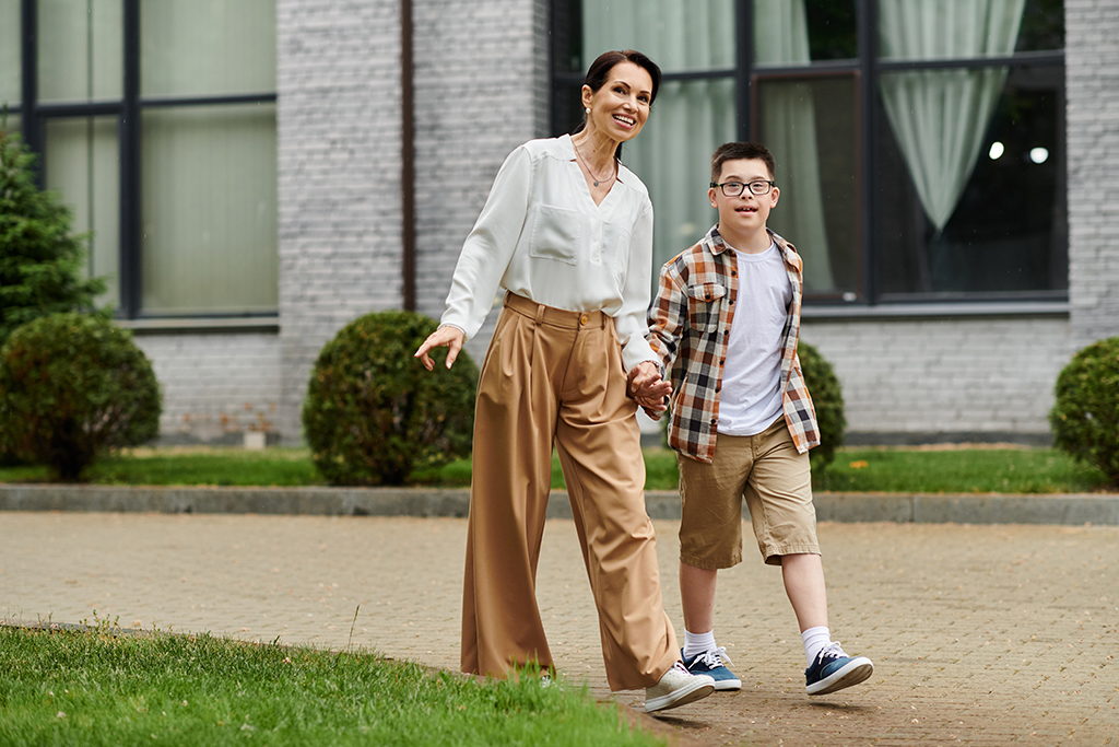A mother and her son with Down syndrome walk hand-in-hand outdoors near an office building, showcasing diversity and inclusion.